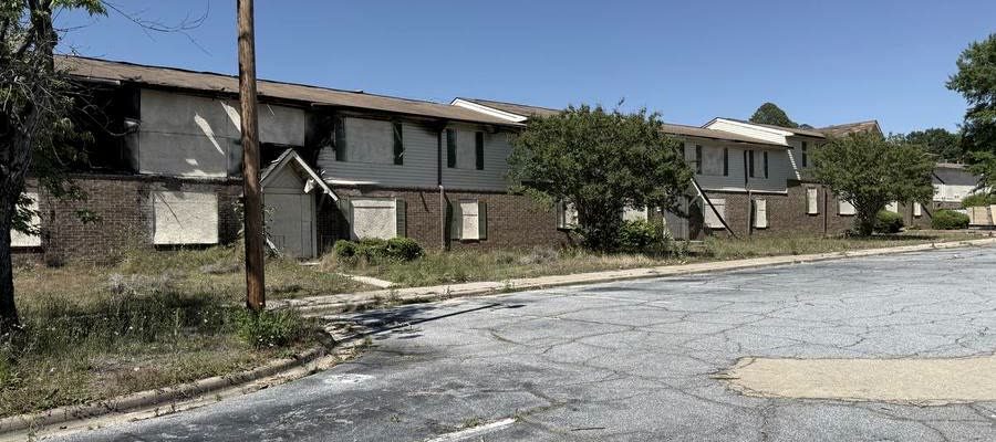 A vacant two-story multifamily building with boarding fitted across doors and windows